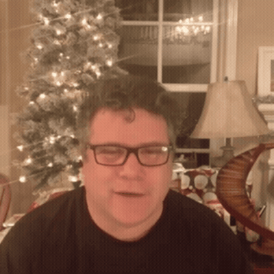 A Man In Front Of A Christmas Tree Wearing Glasses GIF