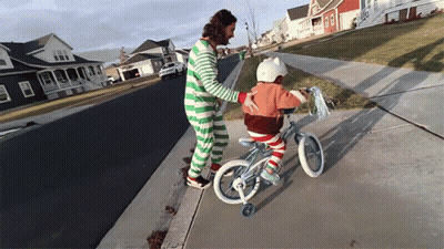 A Man In Green And White Striped Pajamas Helps A Little Girl Ride A Bike GIF
