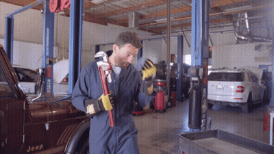 A Man In Overalls Is Holding A Wrench In Front Of A Jeep GIF