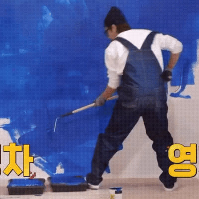 A Man In Overalls Is Painting A Blue Wall With A Roller GIF
