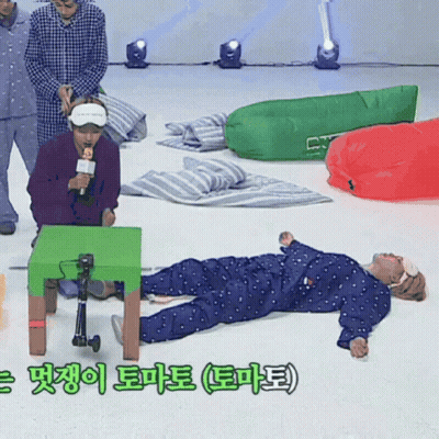 A Man In Pajamas Is Laying On The Floor With A Green Table In The Foreground GIF
