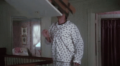 A Man In Pajamas Is Standing On A Staircase Holding A Cardboard Box Over His Head . GIF