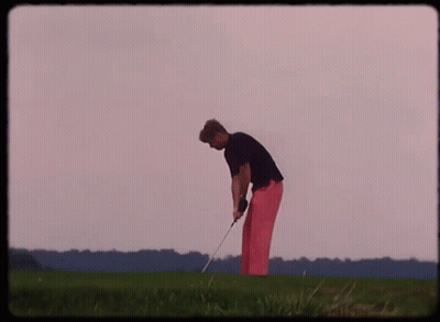 A Man In Pink Pants Is Swinging A Golf Club On A Green Field GIF