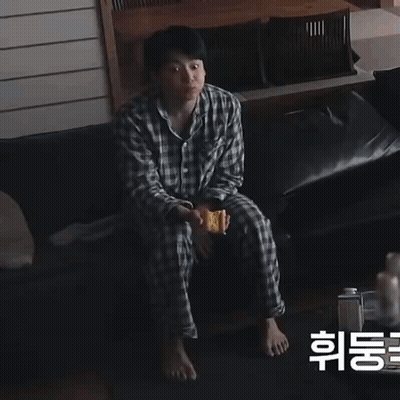 A Man In Plaid Pajamas Sits On A Couch Holding A Sandwich GIF