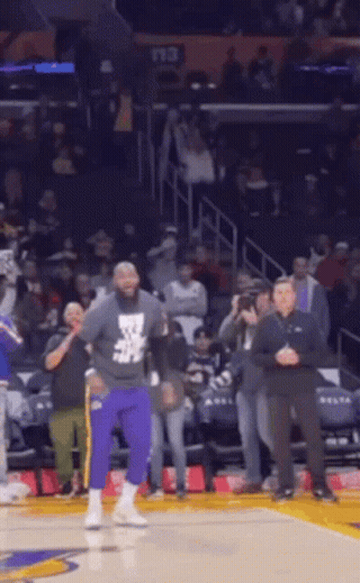 A Man In Purple Pants Is Standing On A Basketball Court In Front Of A Crowd Of People . GIF