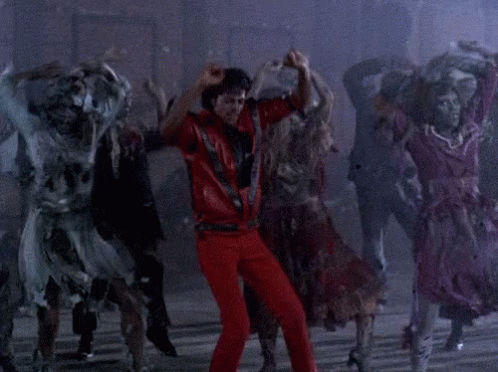 A Man In Red Pants Is Dancing With A Group Of Zombies Behind Him GIF