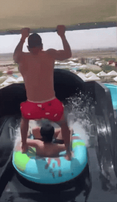 A Man In Red Shorts Is Standing On A Water Slide With Another Man GIF