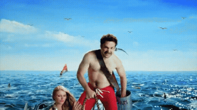 A Man In Red Swim Trunks Is Standing In The Ocean GIF