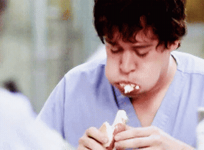 A Man In Scrubs Is Eating A Hot Dog With Cream Cheese GIF