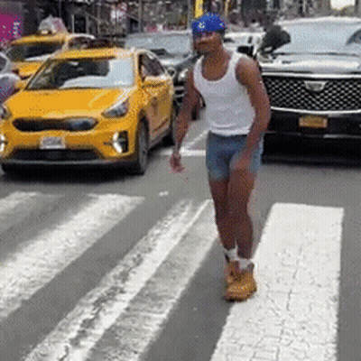 A Man In Shorts And A Tank Top Is Crossing A Street In Front Of A Yellow Car . GIF