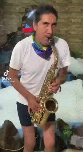 A Man In Shorts Is Playing A Saxophone In Front Of A Waterfall . GIF