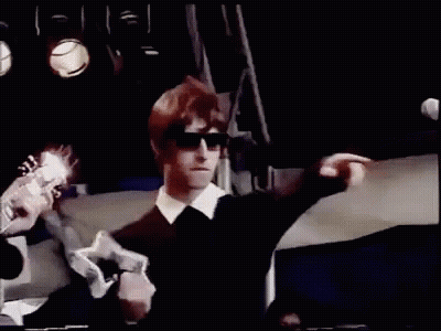 A Man In Sunglasses Is Playing A Guitar On Stage . GIF