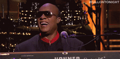 A Man In Sunglasses Is Singing Into A Microphone While Playing A Keyboard . GIF