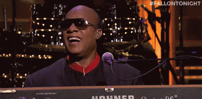 A Man In Sunglasses Is Singing Into A Microphone While Playing A Keyboard . GIF