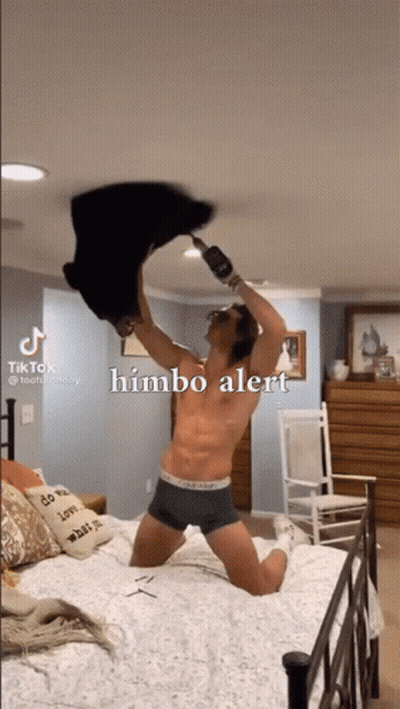 A Man In Underwear Is Kneeling On A Bed With A Bottle Of Wine In His Hand And The Caption Himbo Alert GIF