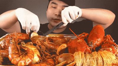 A Man In White Gloves Is Eating A Tray Of Seafood GIF