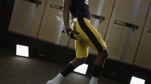 A Man In Yellow Shorts Is Standing In A Locker Room With A Sign That Says ' Nebraska ' On It GIF