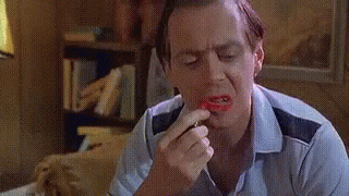 A Man Is Applying Lipstick To His Lips In A Living Room . GIF