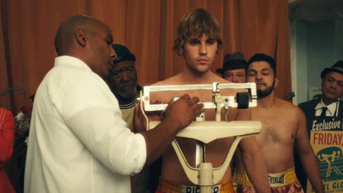 A Man Is Being Weighed On A Scale With A Sign In The Background That Says Exclusive Friday GIF