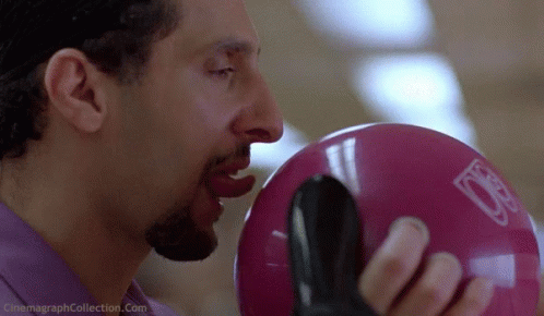 A Man Is Biting Into A Pink Bowling Ball With The Letter D On It GIF