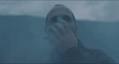 A Man Is Blowing His Nose With A Napkin While Standing In A Dark Room . GIF