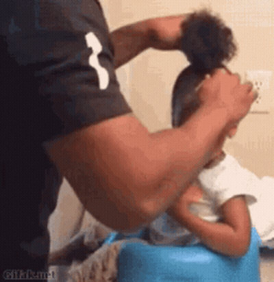 A Man Is Brushing A Little Girl 'S Hair While She Is Sitting On A Blue Chair . GIF