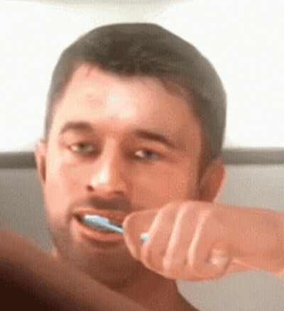 A Man Is Brushing His Teeth With A Blue Toothbrush In Front Of A Mirror . GIF