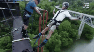 A Man Is Bungee Jumping Off A Bridge While Another Man Helps Him . GIF