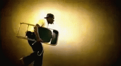 A Man Is Carrying A Chair On His Back In The Dark . GIF
