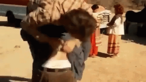 A Man Is Carrying A Child In His Arms While A Group Of People Are Standing Around . GIF