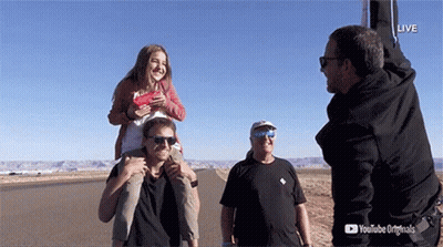 A Man Is Carrying A Girl On His Shoulders While Another Man Watches GIF