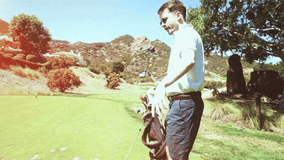 A Man Is Carrying A Golf Bag And A Golf Club On A Golf Course GIF