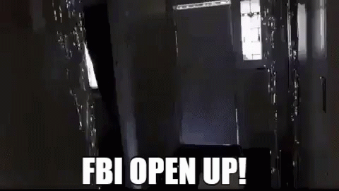 A Man Is Carrying A Large Box In A Hallway With The Words `` Fbi Open Up '' Written On It . GIF