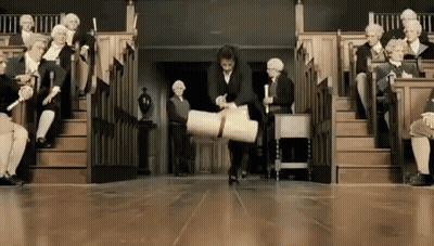 A Man Is Carrying A Large Piece Of Paper In Front Of A Group Of People Sitting In A Lecture Hall . GIF