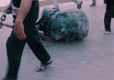 A Man Is Carrying A Large Rock With Chains Around It . GIF