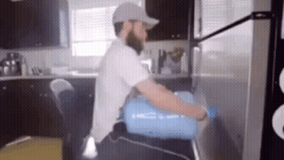A Man Is Carrying A Water Bottle On His Back Into A Refrigerator . GIF