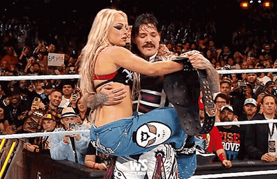 A Man Is Carrying A Woman In A Wrestling Ring With A Crowd Watching . GIF