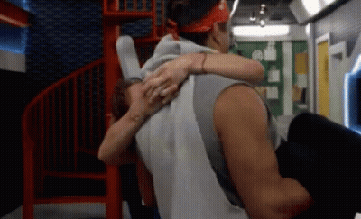 A Man Is Carrying A Woman In His Arms In A Room With A Spiral Staircase GIF