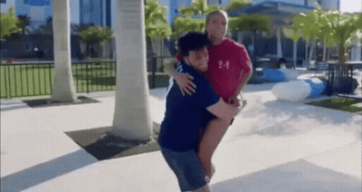 A Man Is Carrying A Woman On His Back In A Park While A Woman Looks On . GIF