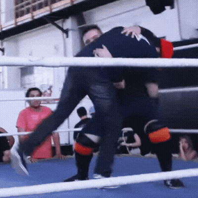 A Man Is Carrying Another Man In A Boxing Ring While Another Man Watches GIF