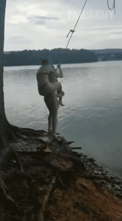 A Man Is Carrying Another Man In His Arms Into The Water . GIF
