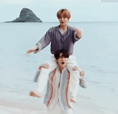 A Man Is Carrying Another Man On His Shoulders In The Water GIF