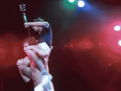 A Man Is Carrying Another Man On His Shoulders On A Stage While Holding A Guitar . GIF