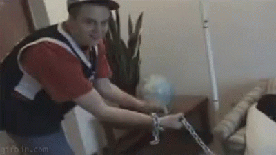 A Man Is Chained To A Table With A Chain Around His Ankle . GIF