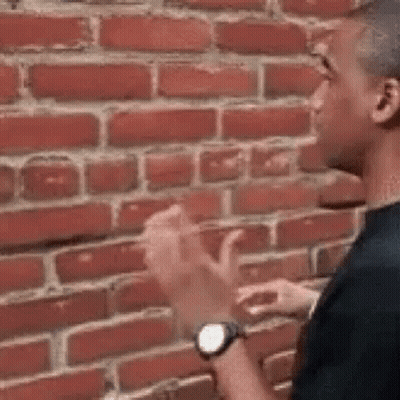A Man Is Clapping His Hands In Front Of A Brick Wall While Wearing A Watch . GIF