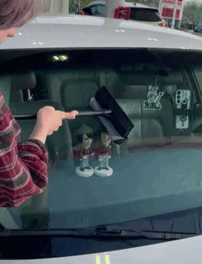 a man is cleaning the windshield of a car with a wiper and two bobbleheads on it