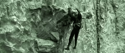 A Man Is Climbing A Rock Wall With A Rope . GIF
