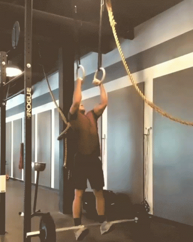 A Man Is Climbing A Rope In A Gym With A Rogue Sign Behind Him GIF