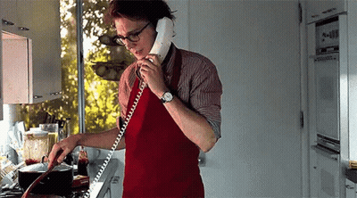 A Man Is Cooking In A Kitchen While Talking On A Phone . GIF