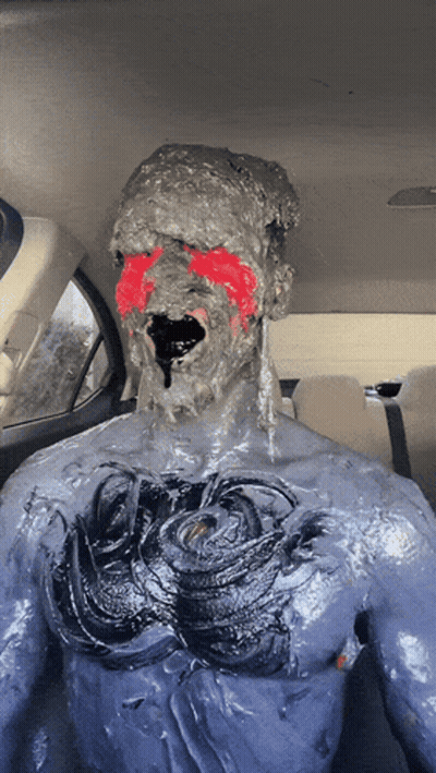 A Man Is Covered In A Thick Gray Substance With Red Paint On His Face GIF